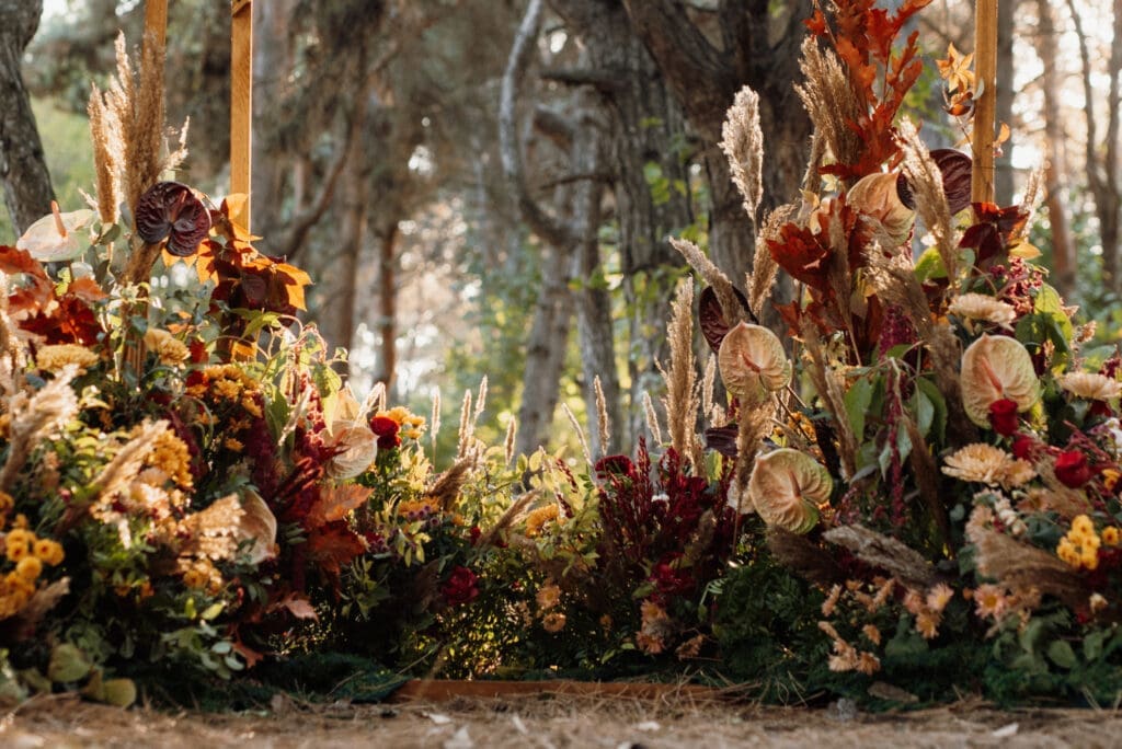 Lush wedding ceremony floral installation with dried flowers and grasses in a pine forest setting