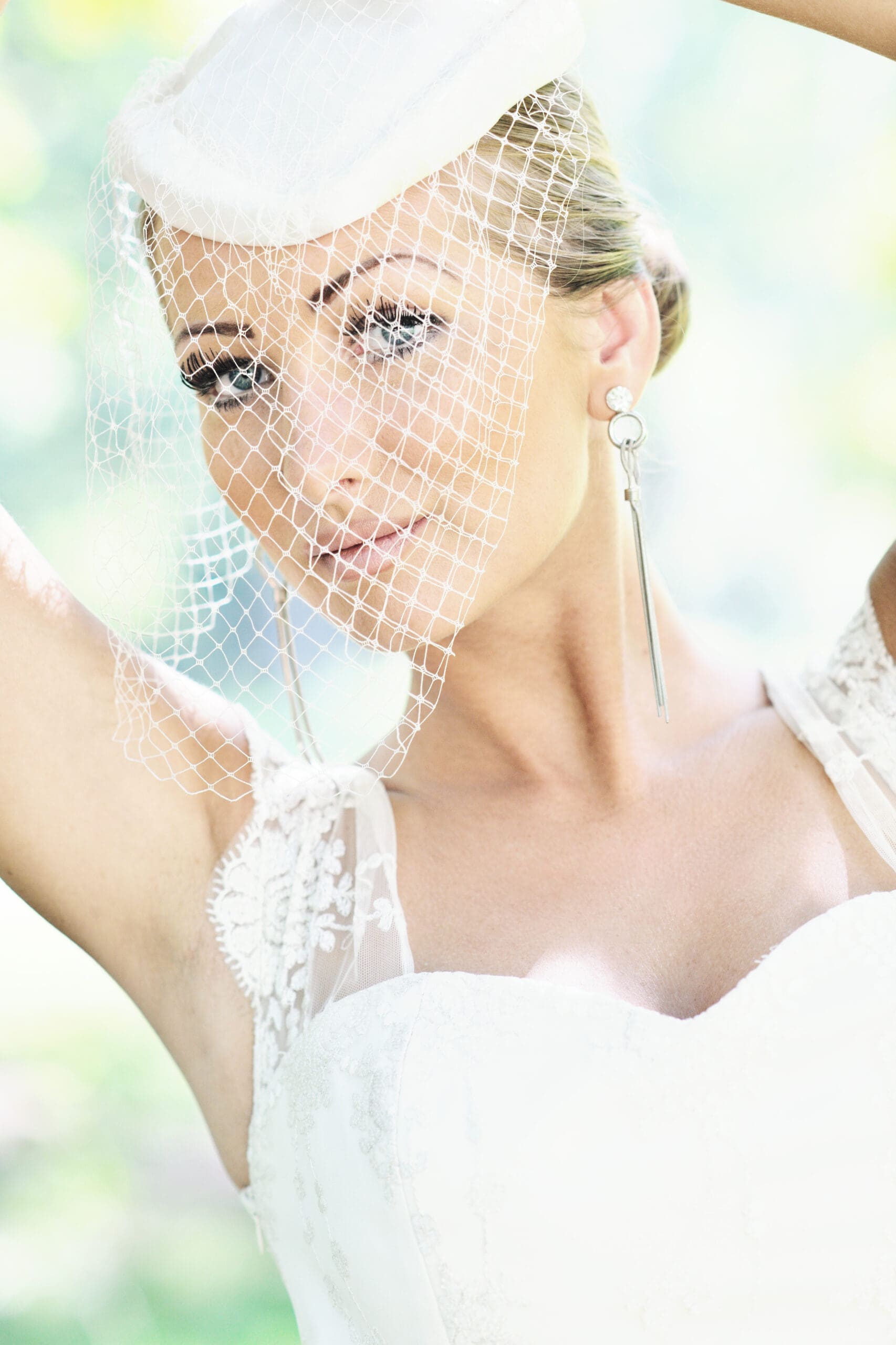 Bride wearing a white fascinator with birdcage netting, styled in a soft bridal updo