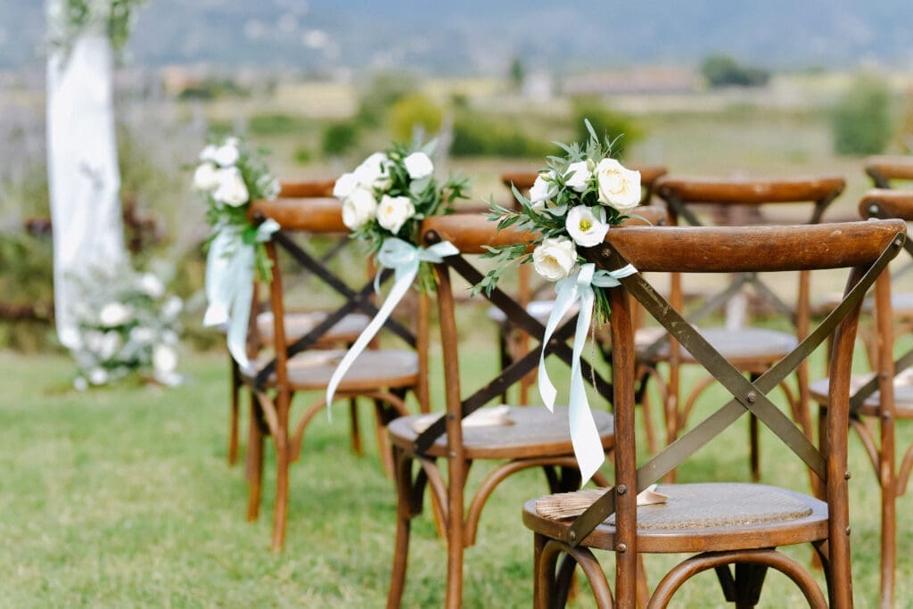 Row of wooden wedding ceremony chairs decorated with white flowers and ribbon