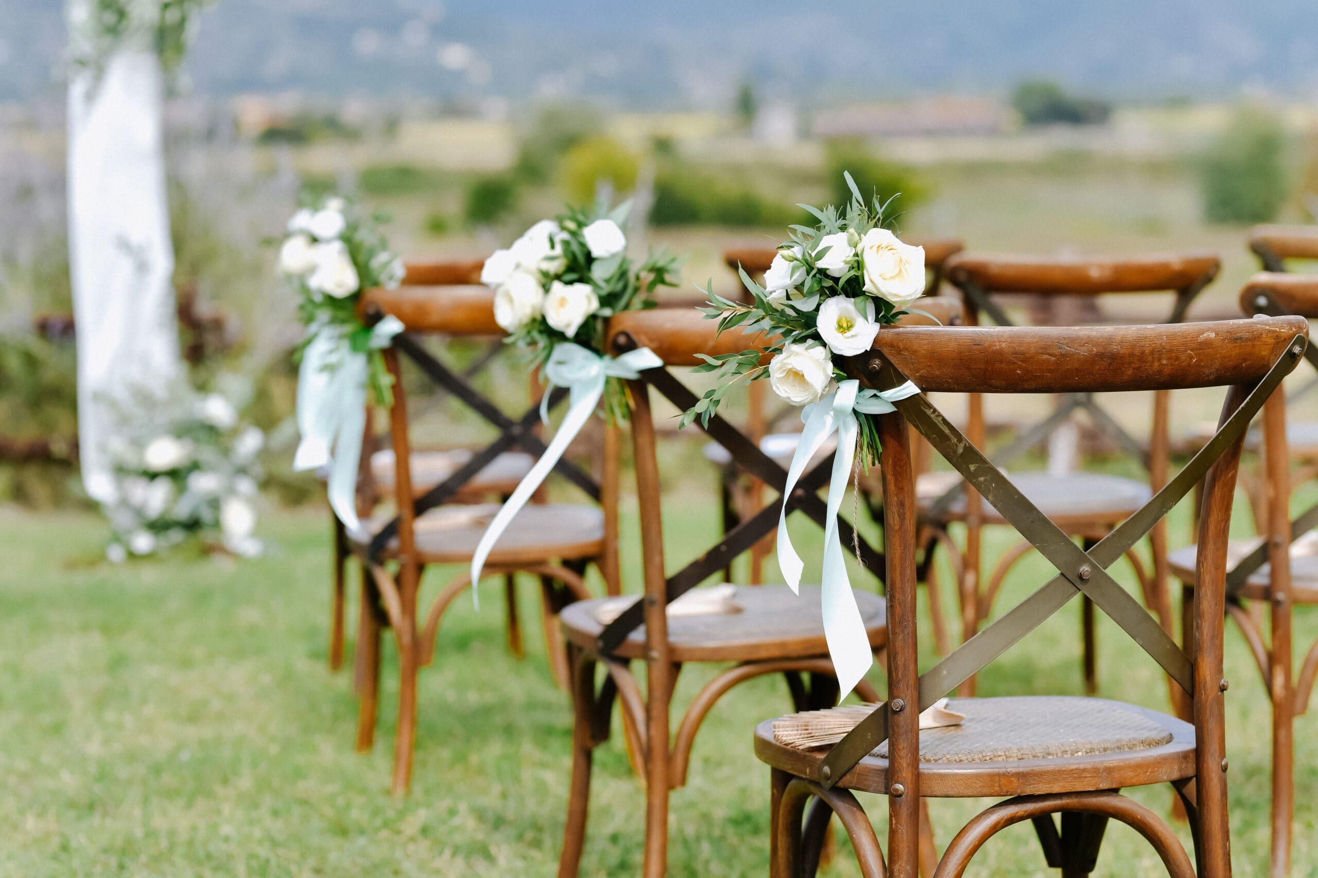 Row of wooden wedding ceremony chairs decorated with white flowers and ribbon